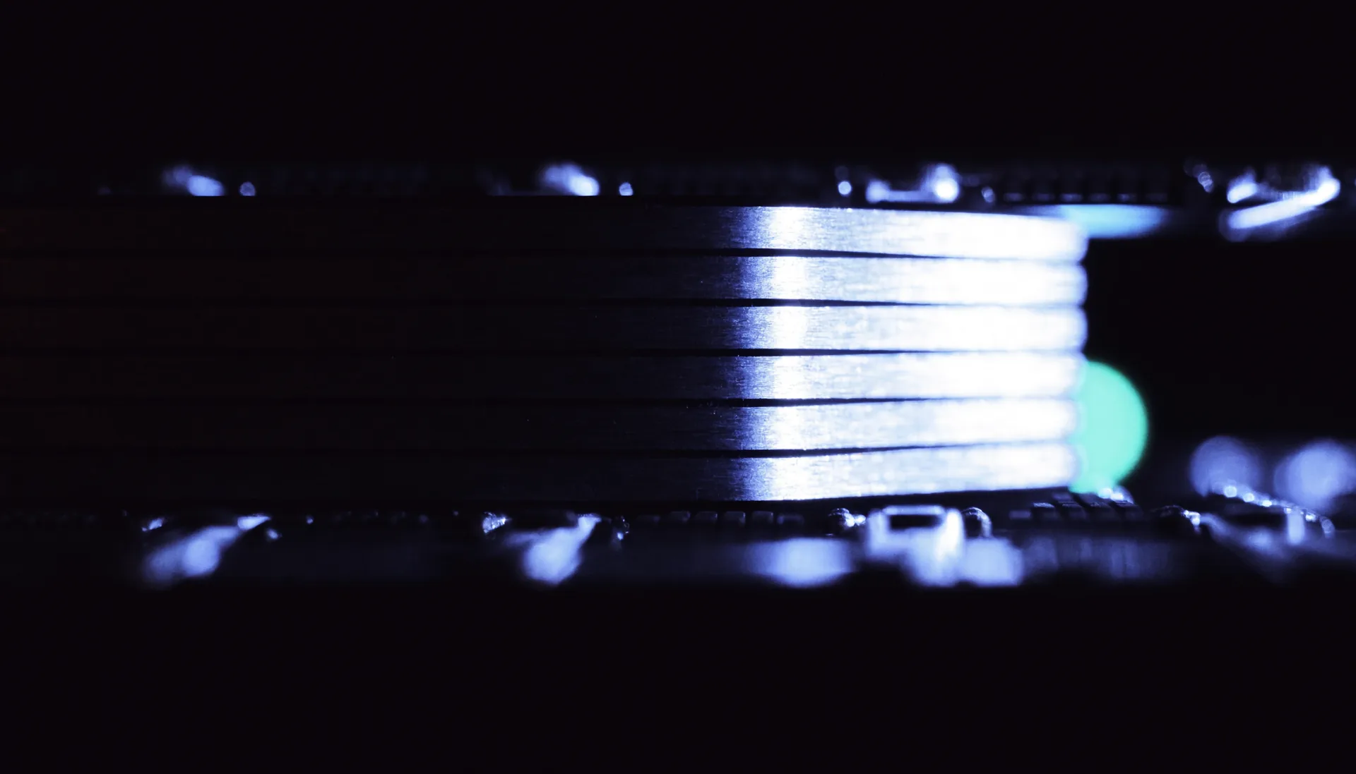 Machined heatsink fins and the edge of a circuit board, lit by one cold light.